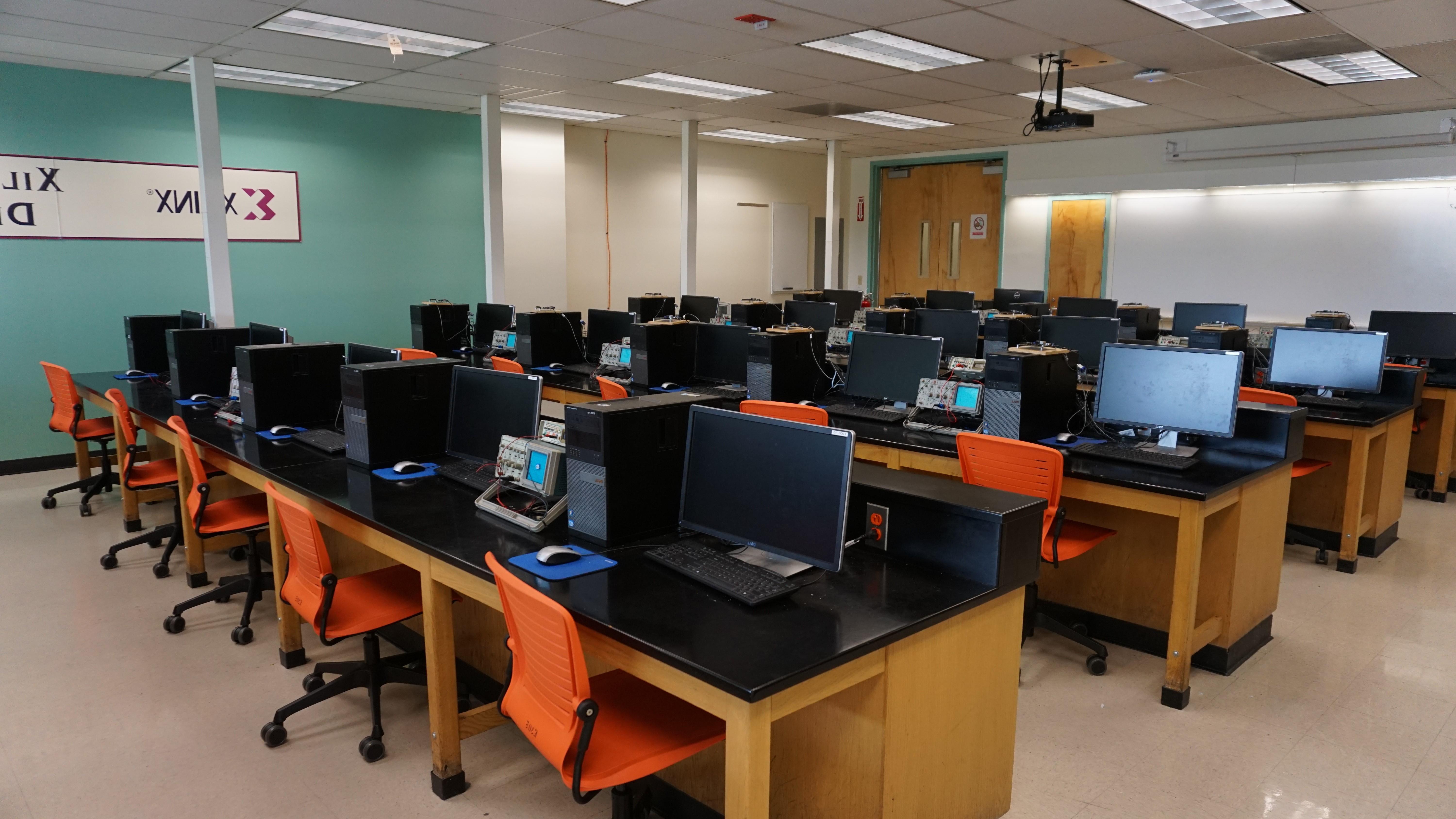 A classroom with computers, orange chairs, and a bright teal wall with the Xilinx logo.